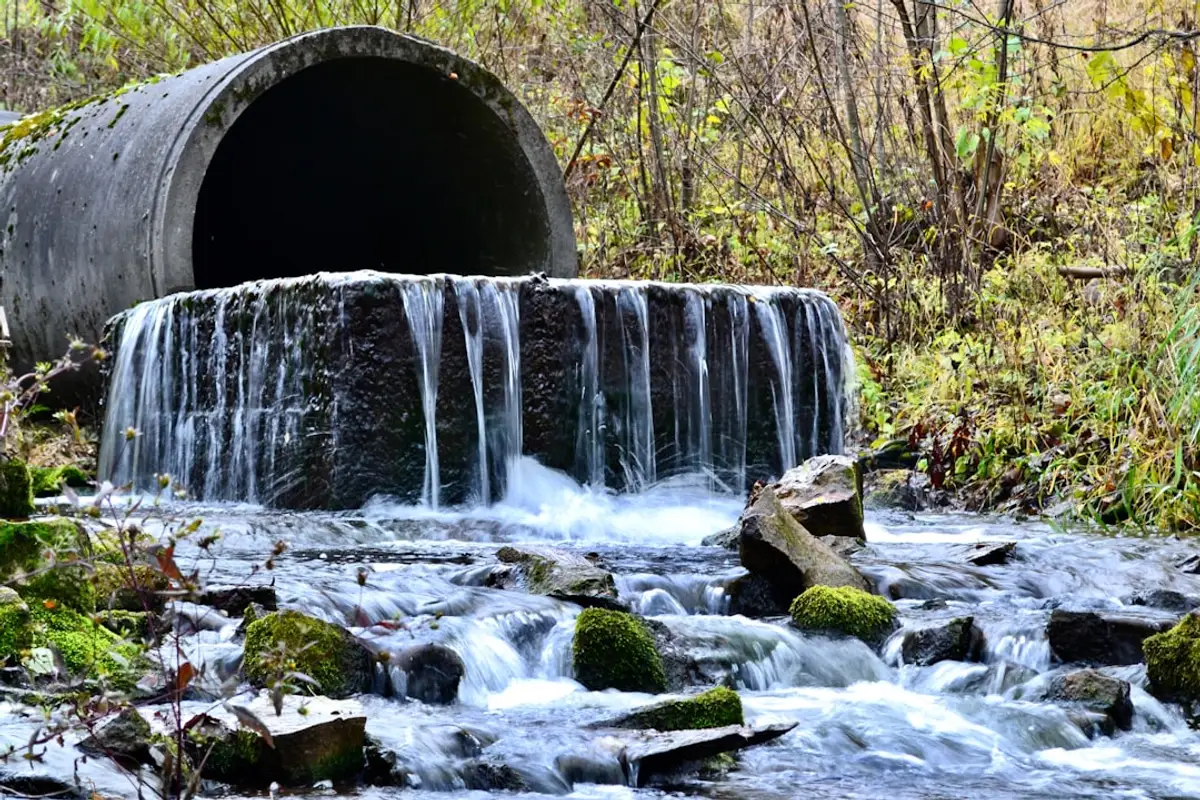 Concrete culvert outfall with rock bags at the apron, water flowing